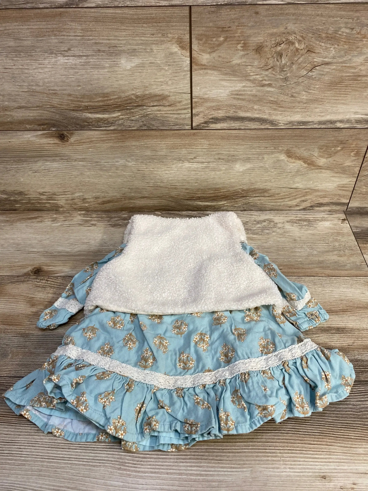 Blue floral baby dress with white lace trim and soft white fleece vest on wooden floor