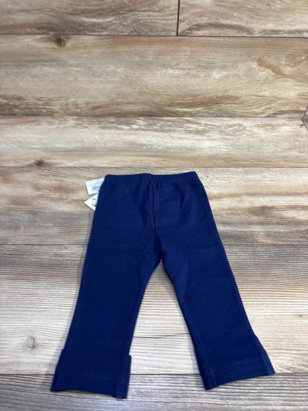 Flat lay of navy blue baby leggings size 6-9M showing elastic waistband and small side hem slits on wood background