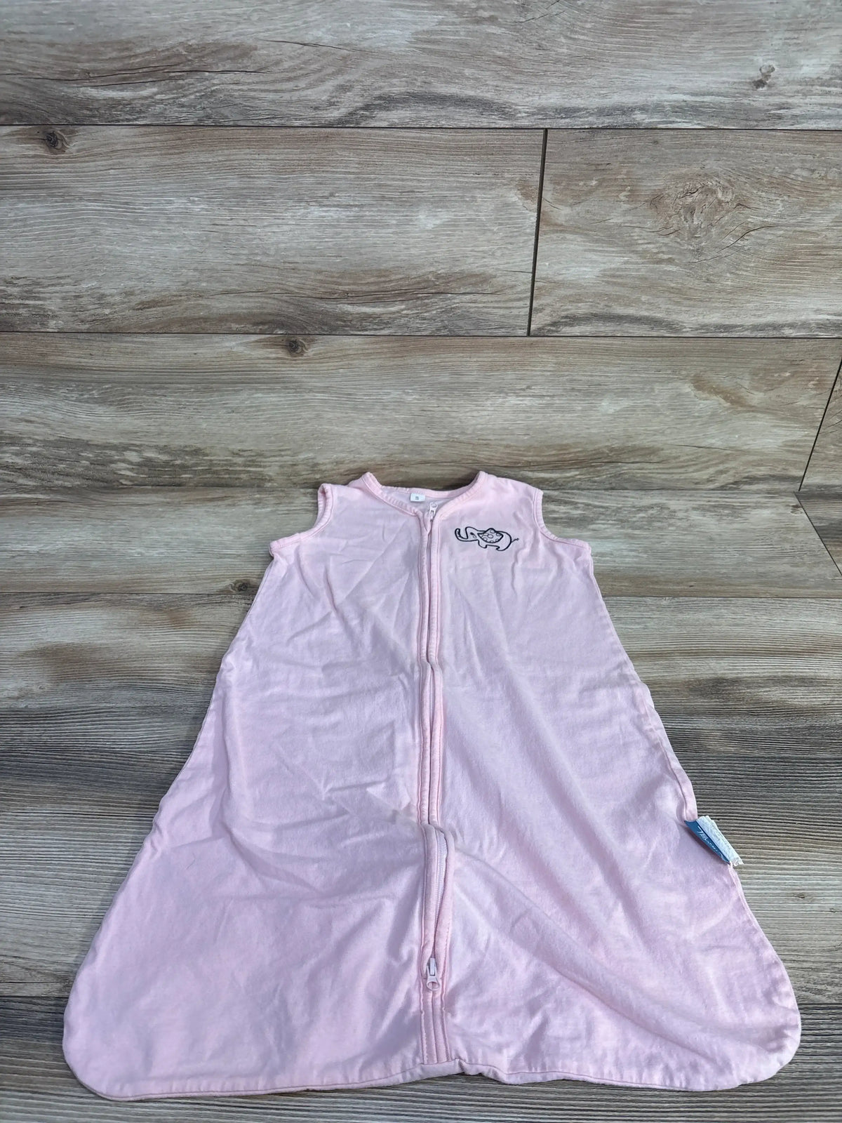 Flat lay of pink Tillyou elephant sleep sack size 0-6 months showcasing front zipper and elephant embroidery on wood floor background