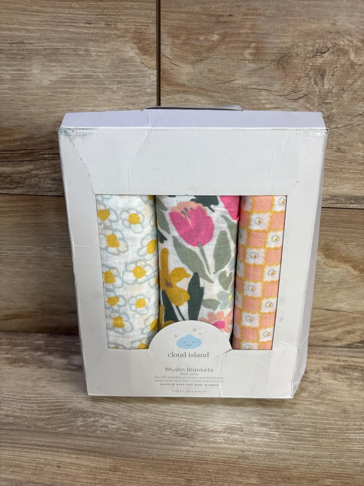 Front view of Cloud Island 3-pack muslin swaddle blankets showing three patterned blankets in white box on wood background