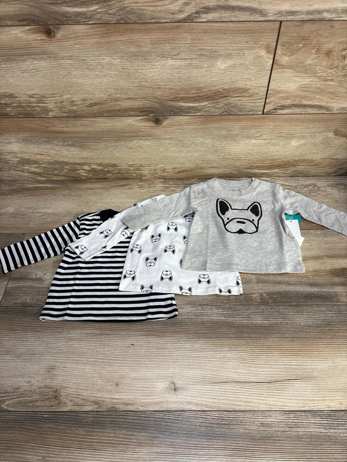 Flat lay of NEW Mighty Goods 3pk Dog Print Shirts sz 3m showcasing grey french bulldog graphic dog face print and navy stripe long sleeve tops on wood floor