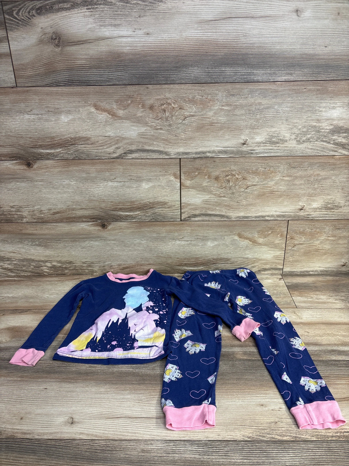 Children's blue pajama set with pink cuffs featuring castle and heart designs on wooden background