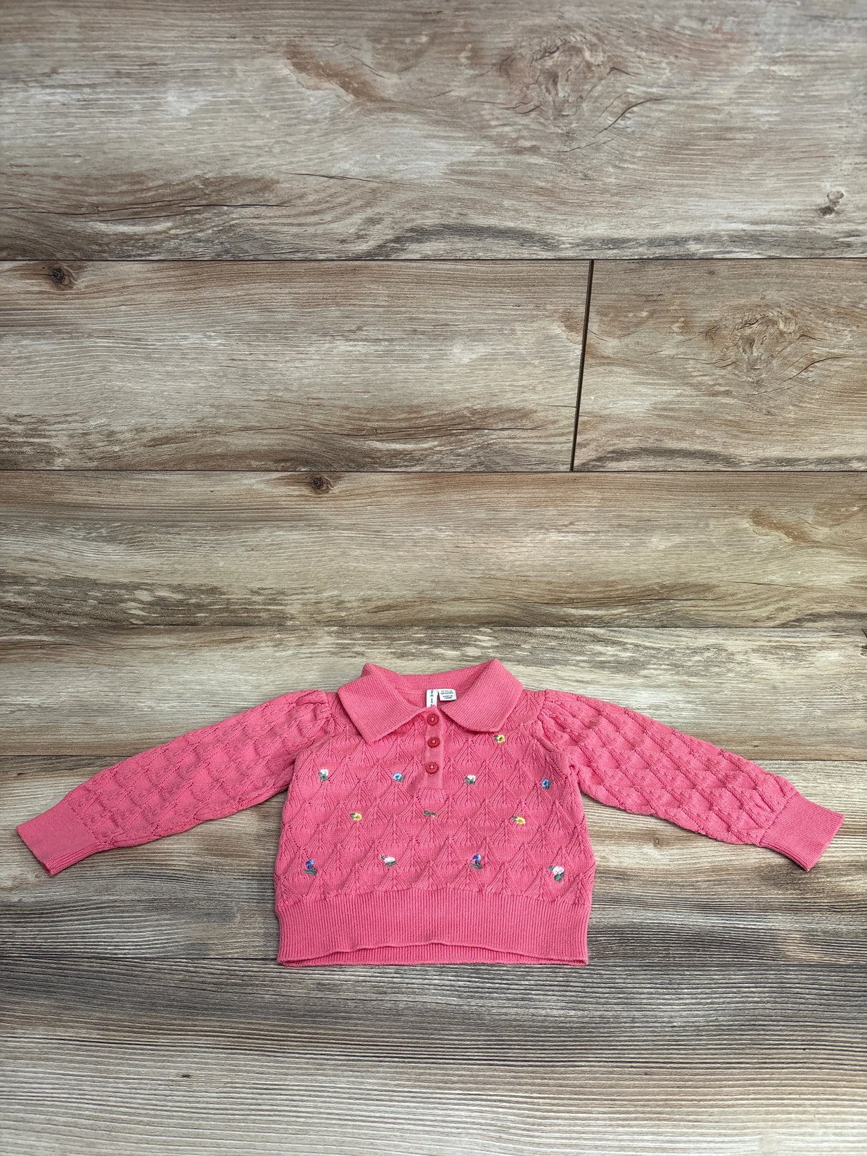 Pink toddler sweater with collar and colorful embroidered patterns, laid flat on wood floor