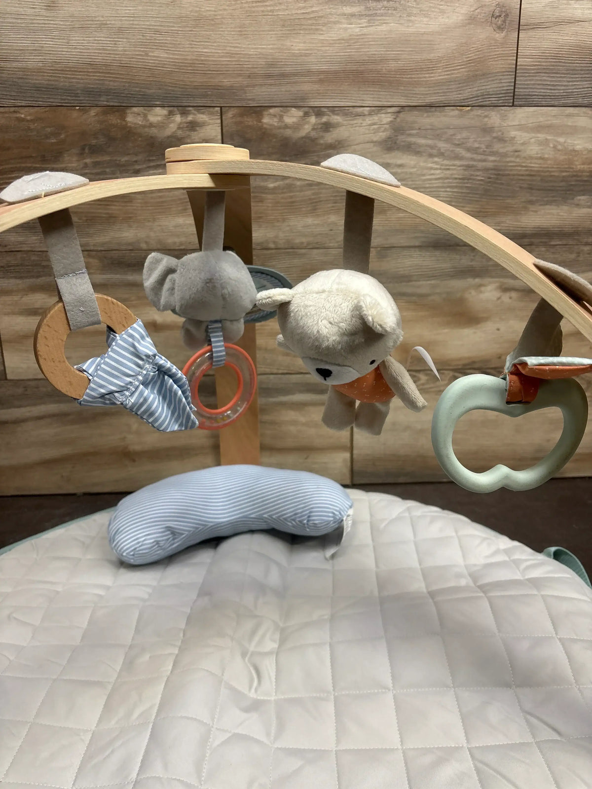 Wooden baby play gym with plush animal toys and a soft playmat on a wood background