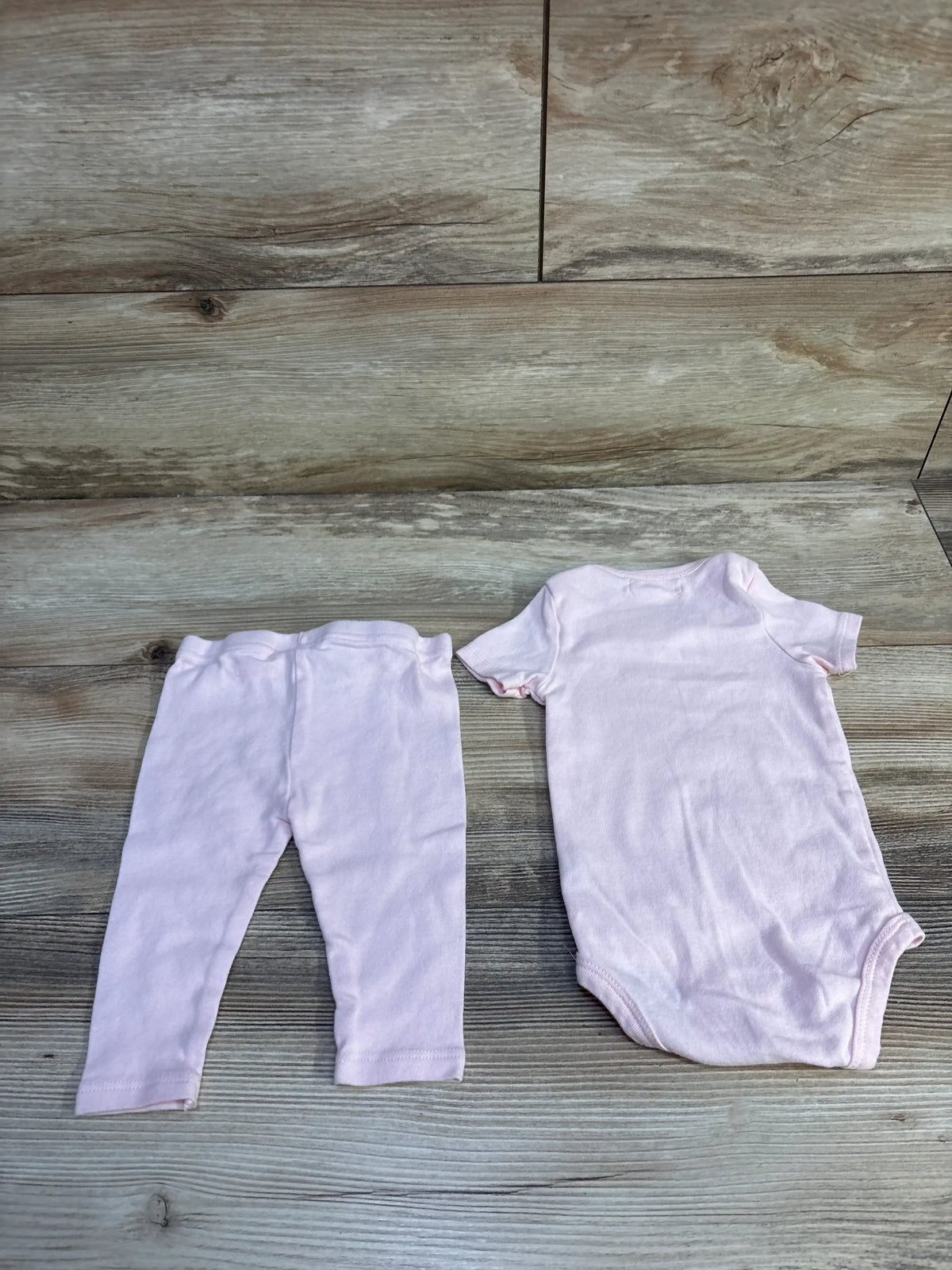 Top down view of the Starting Out pink two piece bodysuit and pants set showcasing the coordinated outfit on a wood look floor