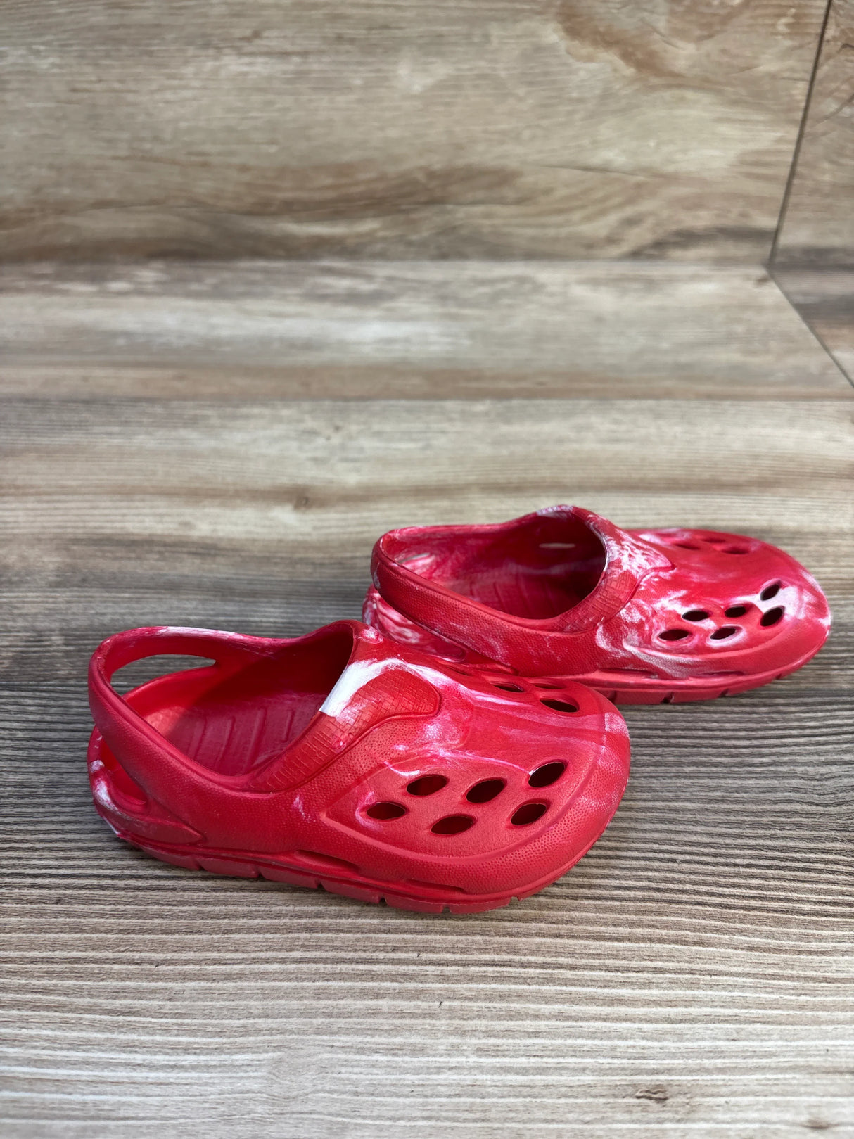 Angled view of red tie-dye toddler clogs size 5C showing molded ventilation holes and back heel strap on light wood background