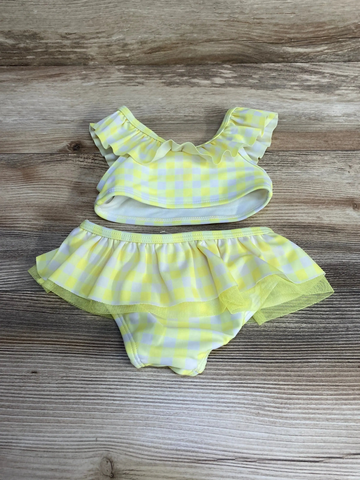 Flat lay of yellow gingham two-piece baby swimsuit size 12m showing ruffled top and skirted bottoms with tulle trim on wood background