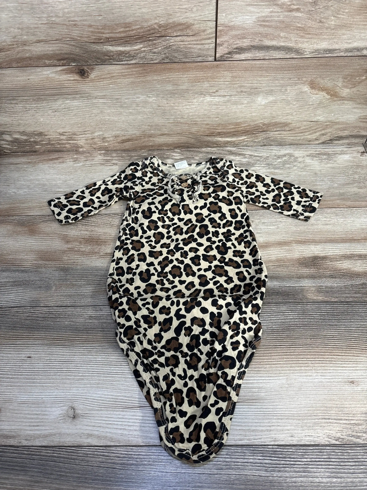 Flat lay of leopard print knotted baby gown with long sleeves showing knotted bottom on wood background