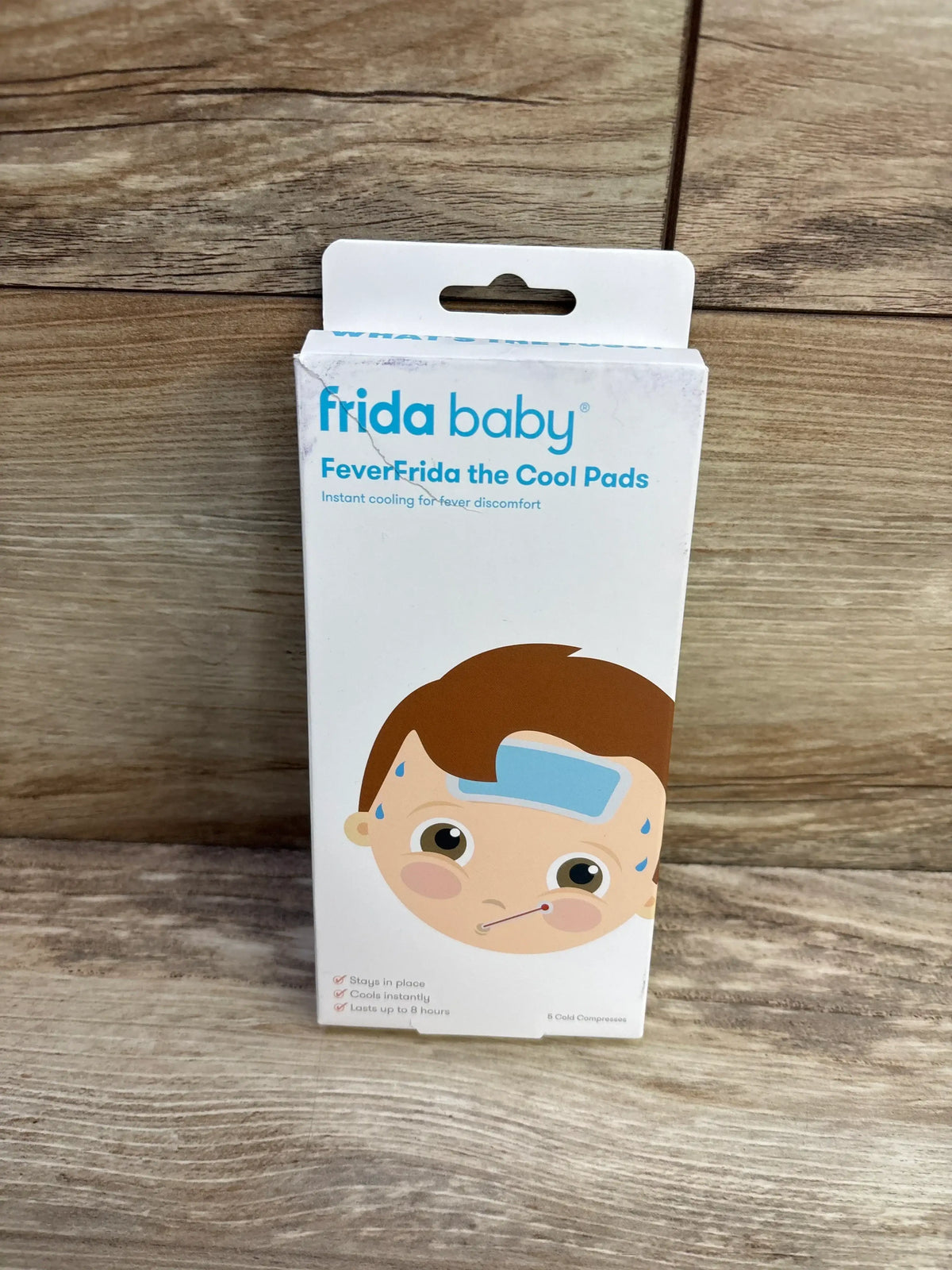 Front view of Frida Baby FeverFrida the Cool Pads 5-pack box showing packaging front with cartoon child and cooling pad on wooden background