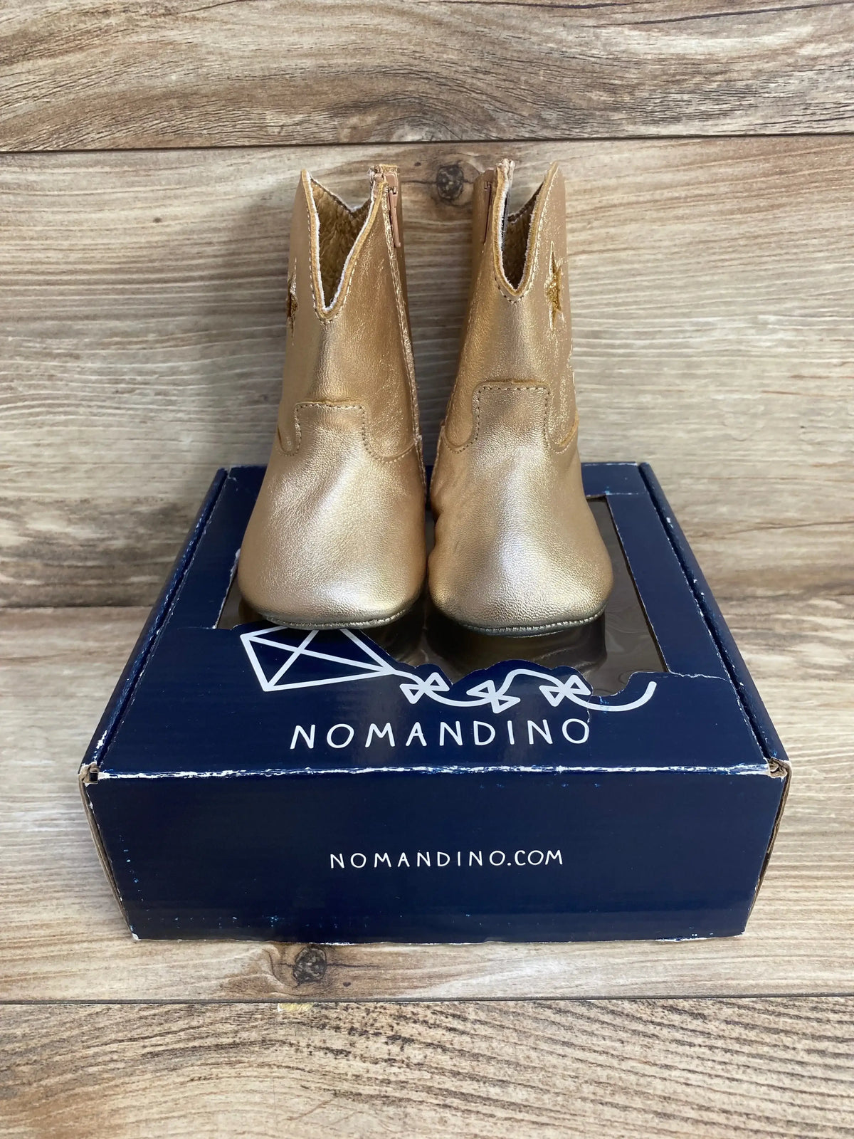 Front view of Nomandino infant gold metallic boots with star cutouts and side zippers on navy box
