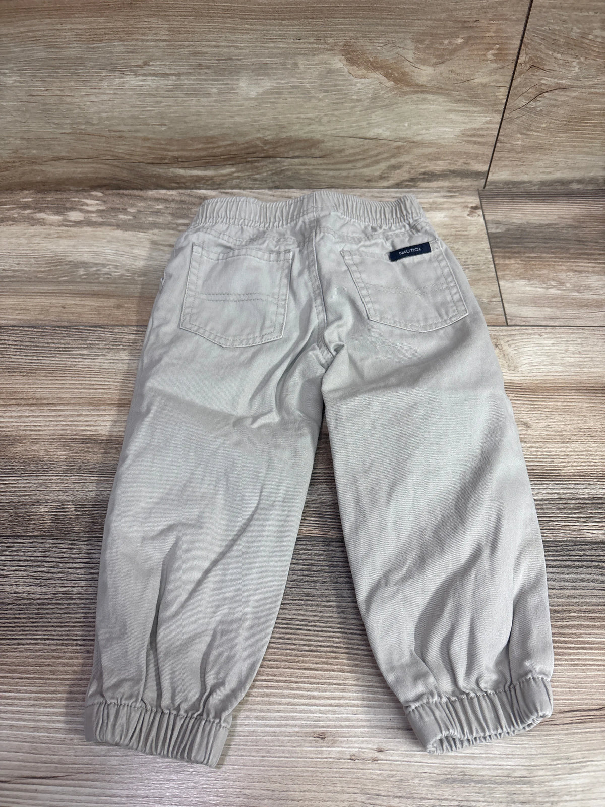 Rear view of Nautica khaki pull-on pants showcasing elastic waistband, cuffs, and two back pockets with wood background