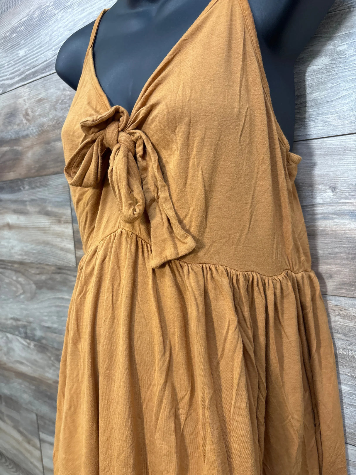 Side close-up of yellow maternity sleeveless dress showing front tie and gathered waist on black mannequin, wood background