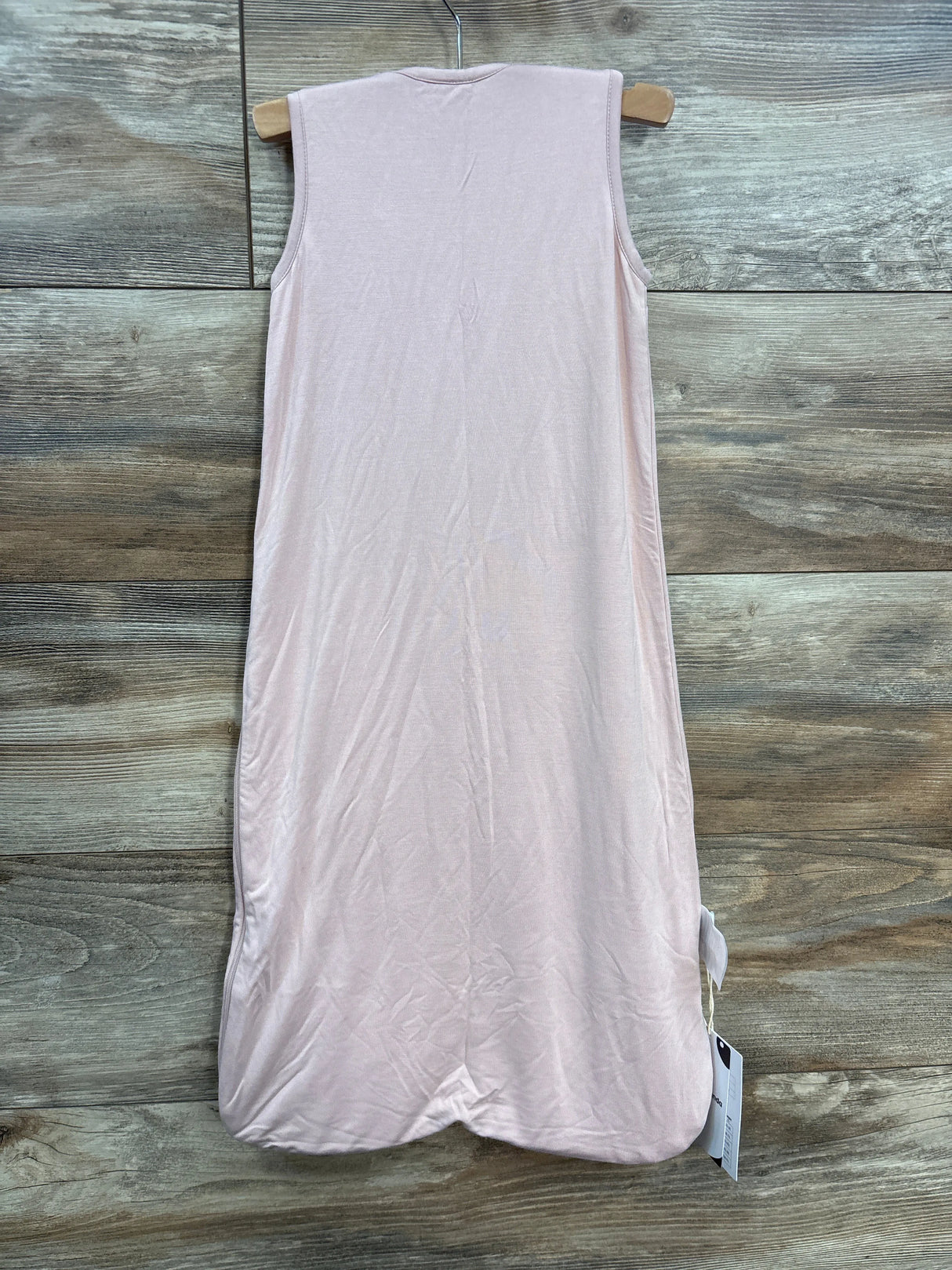 Light pink sleeveless baby sleep sack on a wooden hanger, wood background