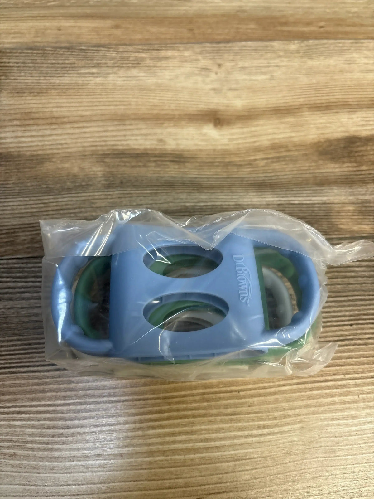 Top view of Dr. Brown’s silicone narrow baby bottle handles 3-pack with blue and green handles in clear plastic packaging on wood surface