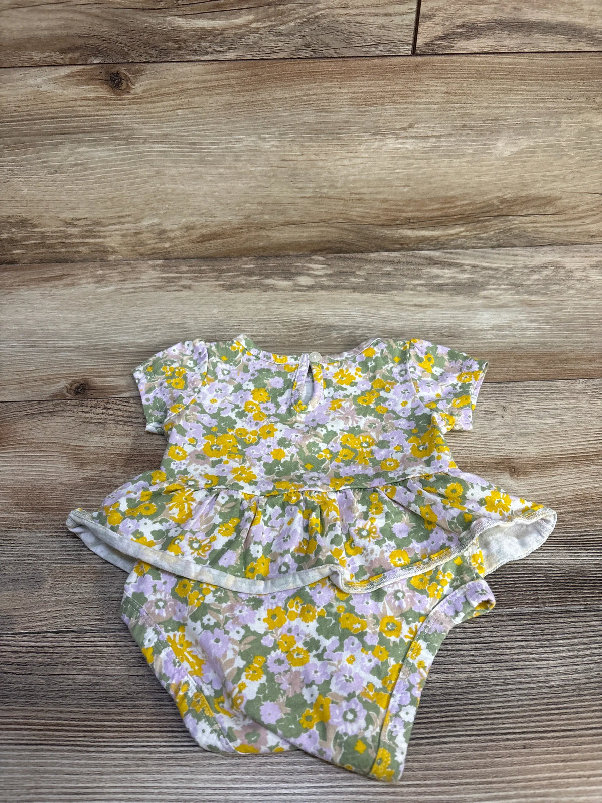Flat lay of Carter's green floral skirted bodysuit showing short sleeves, peplum skirt, and snap closures on wood background