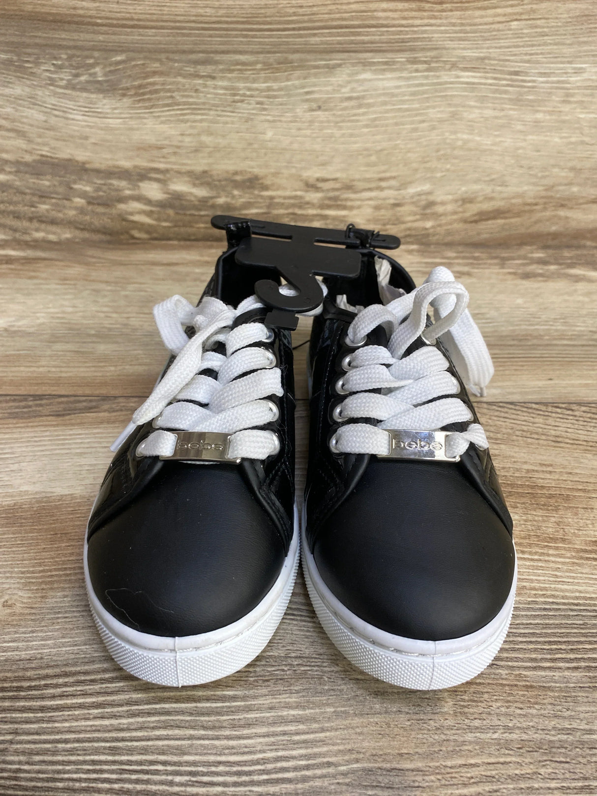 Front view of Bebe Chiara platform sneakers size 12C with black upper, white laces, white platform sole and bebe metal lace tag on wood floor