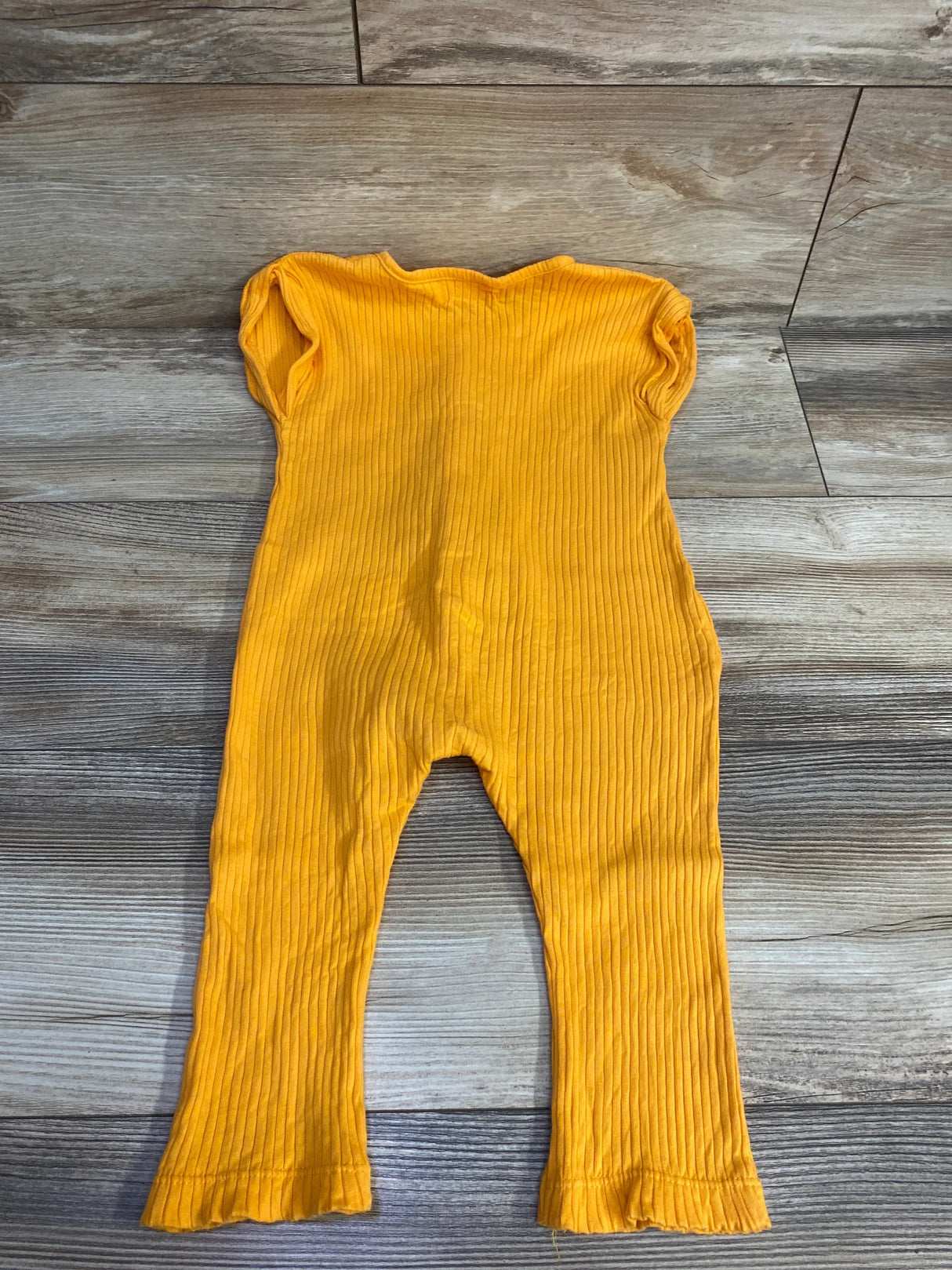 Yellow ribbed baby romper with short sleeves laid on wooden floor