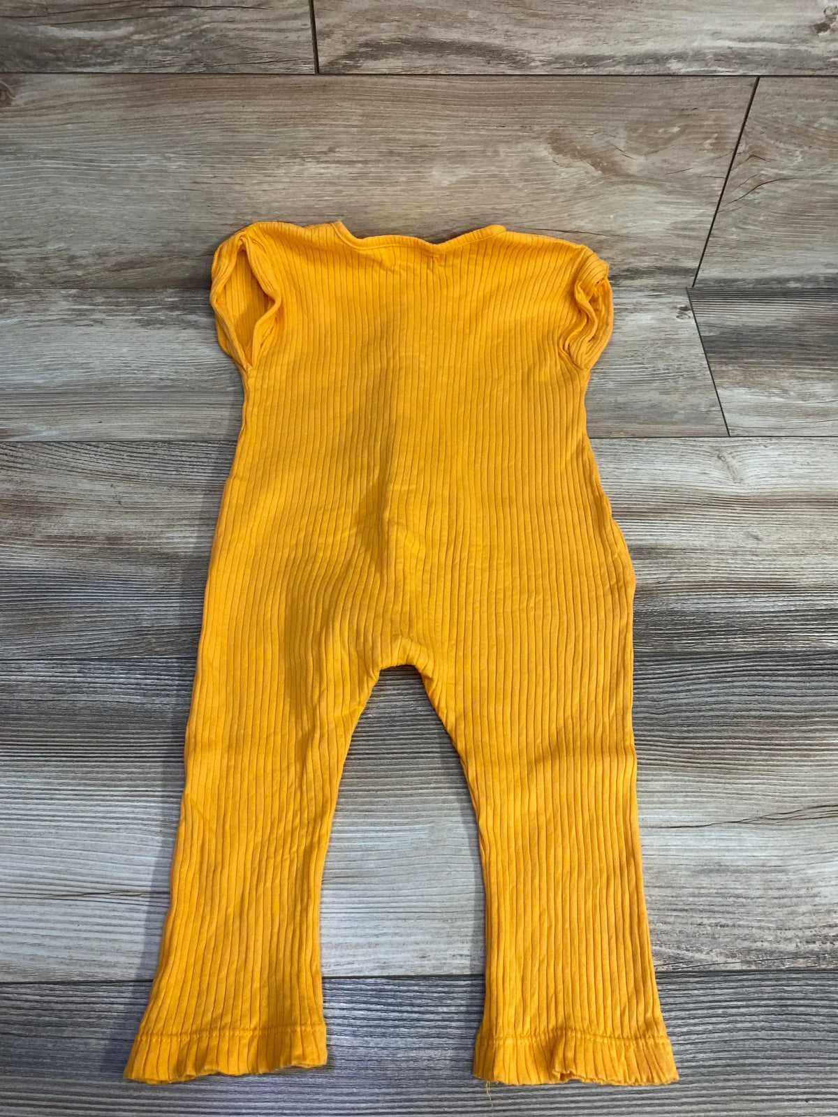 Yellow ribbed baby romper with short sleeves laid on wooden floor