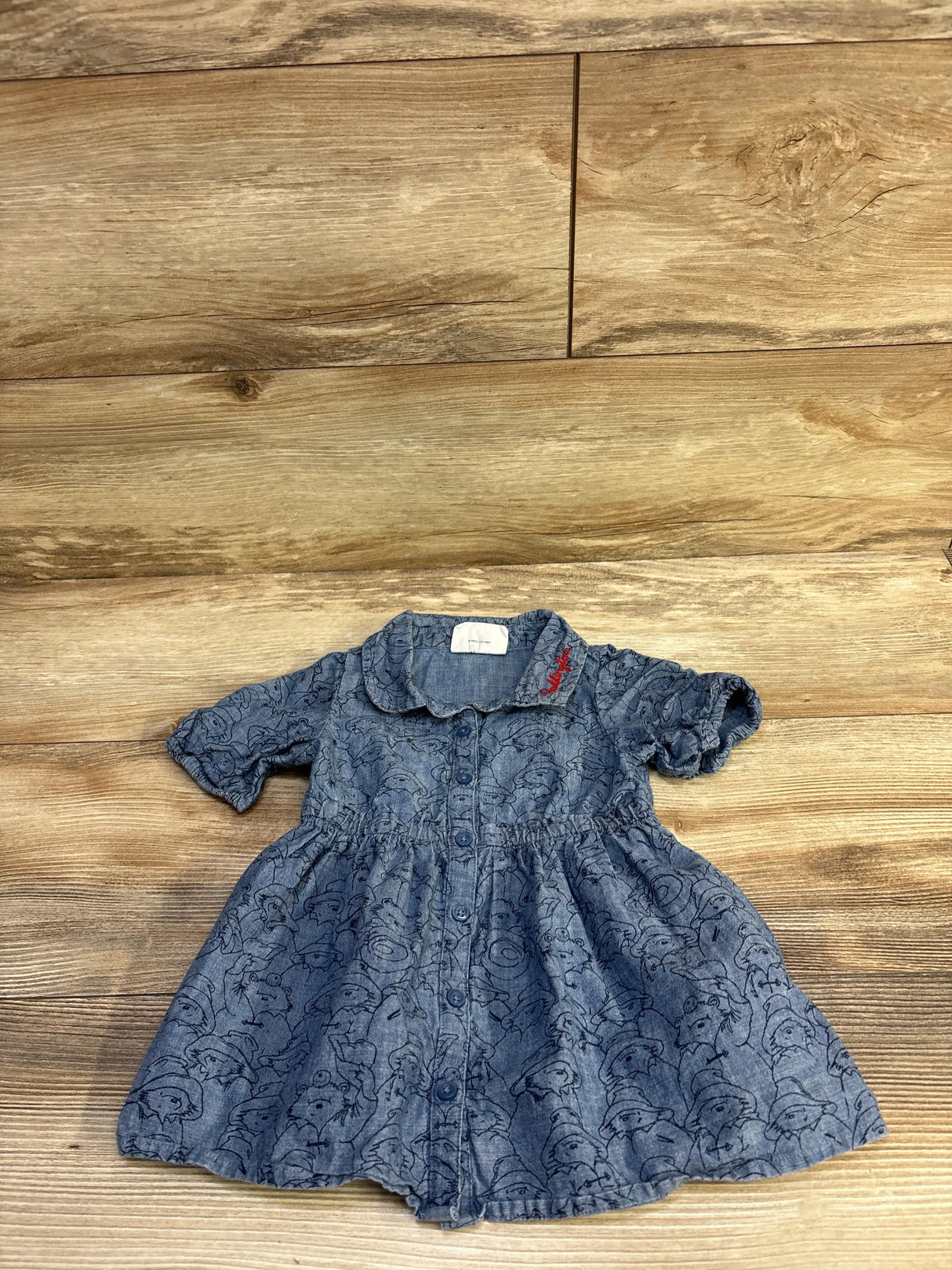 Flat lay of Baby Gap chambray baby dress showing front button placket, Peter Pan collar, short puff sleeves and Paddington bear print on wood background