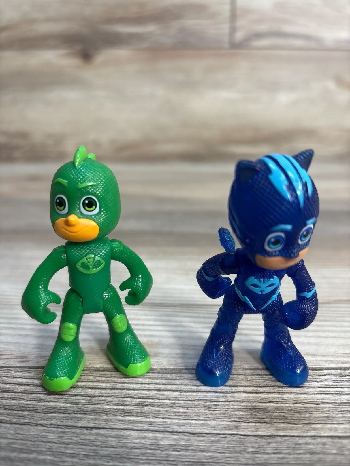 Front view of PJ Masks Catboy and Gekko action figures two-pack showing textured suit details and painted faces on a wood floor background