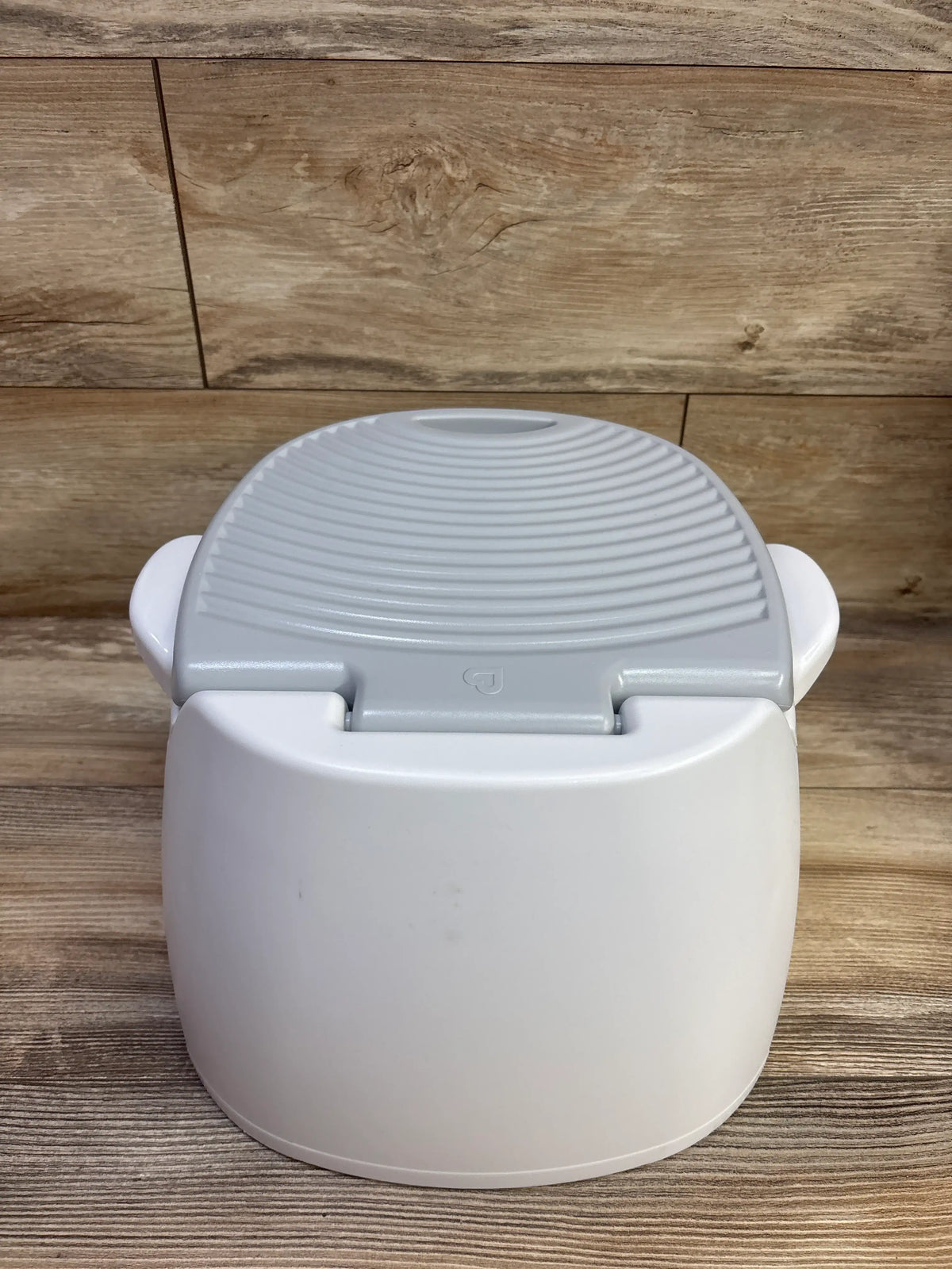 Angled view of Munchkin Arm & Hammer Multi-Stage 3-in-1 Potty showcasing its gray textured lid and white body against wood