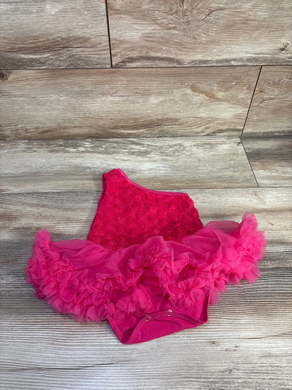 Angled view of London Store one-shoulder tutu bodysuit in soft pink showcasing rose tulle skirt on wood flooring