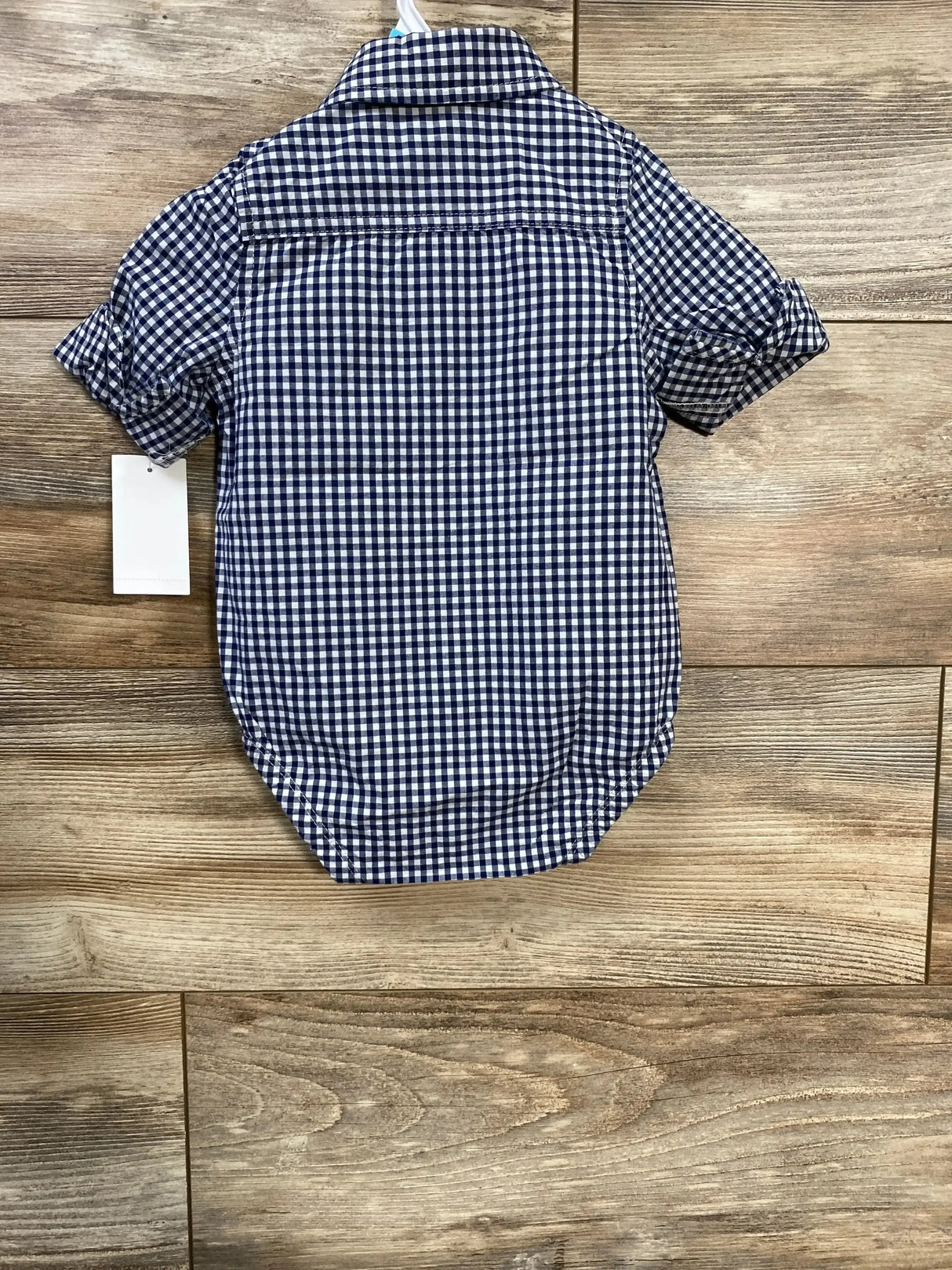 Back view of OshKosh navy gingham button-up bodysuit showing short sleeves, fold-over collar, and snap bottom on wood background