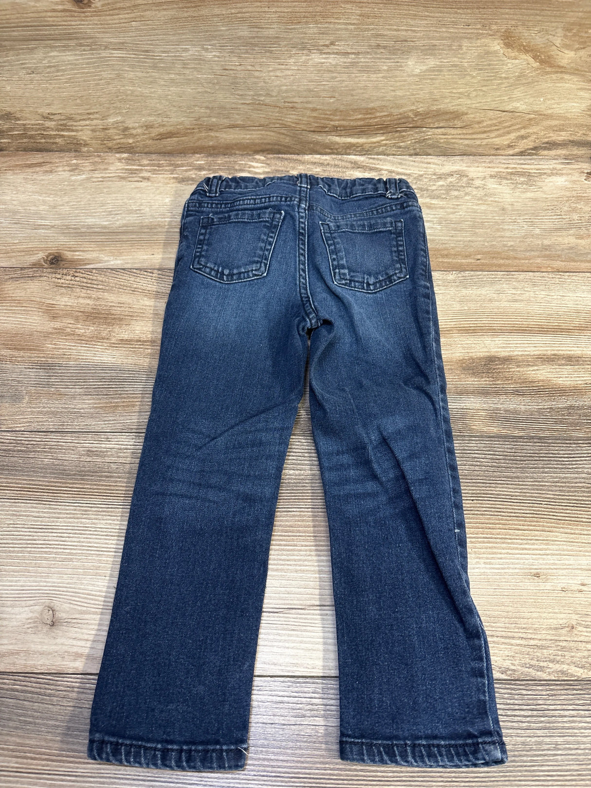 Back view of toddler size 4T Okie Dokie blue jeans showing elastic waistband and two back pockets on wooden floor