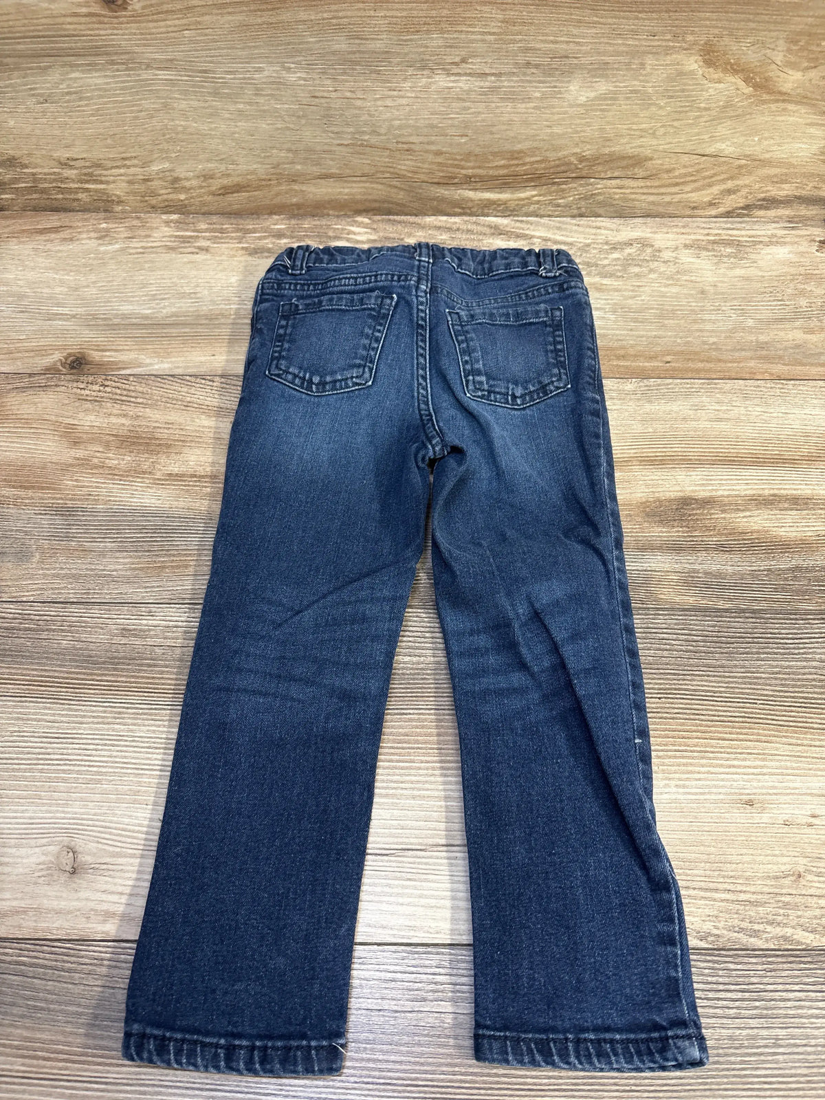 Back view of toddler size 4T Okie Dokie blue jeans showing elastic waistband and two back pockets on wooden floor