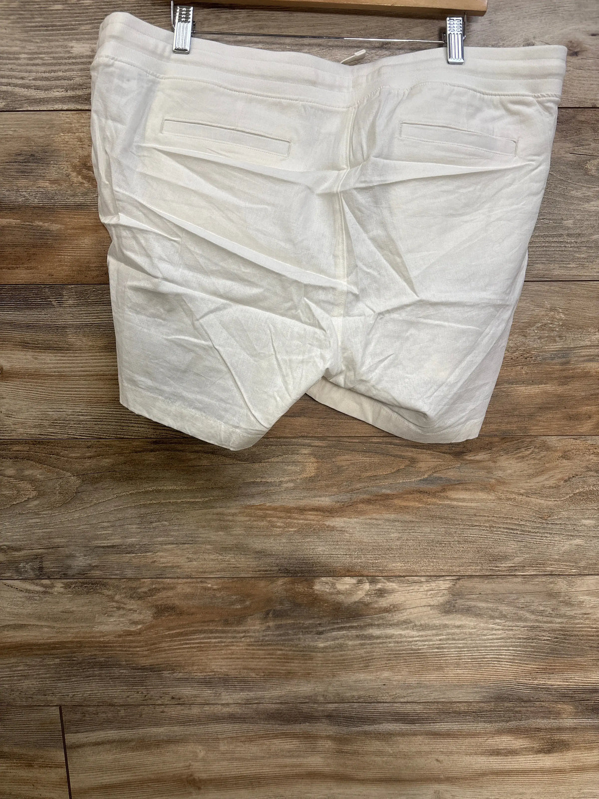 Rear view of white Gap maternity linen-blend shorts showcasing back welt pockets and elasticized under-belly waist on a wood floor