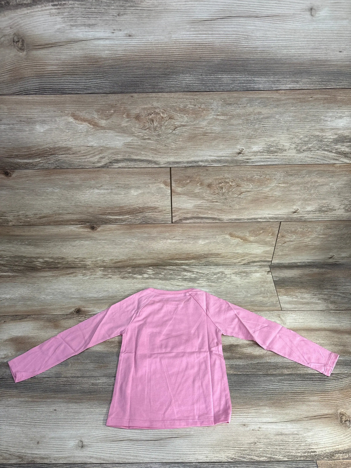 Back view of pink long sleeve shirt laid flat on grey wood plank floor