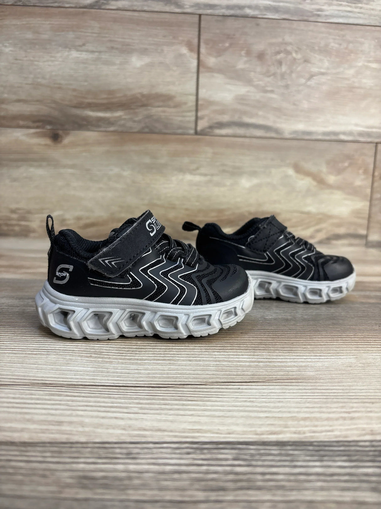 Black kids athletic sneakers with white soles on wood floor