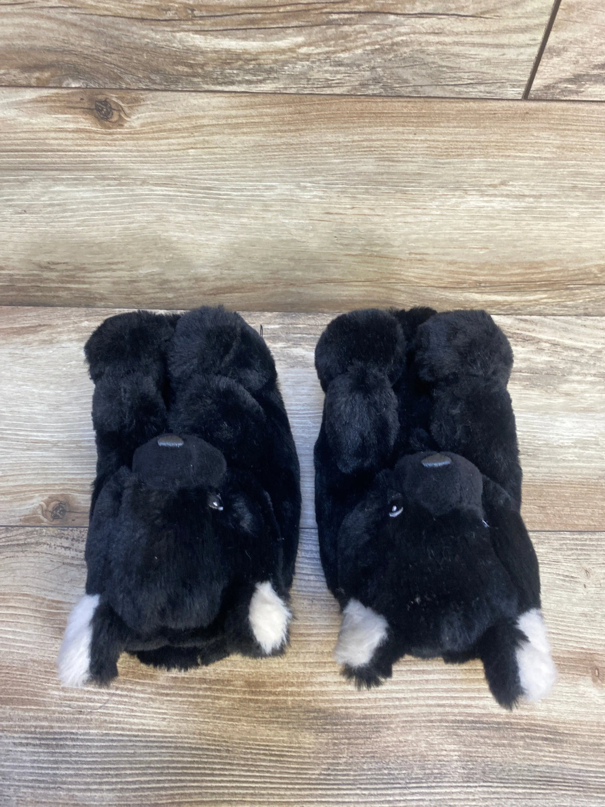 Top-down view of Gap Cozy Bear toddler slippers showcasing black plush bear design with white ear accents on wood floor