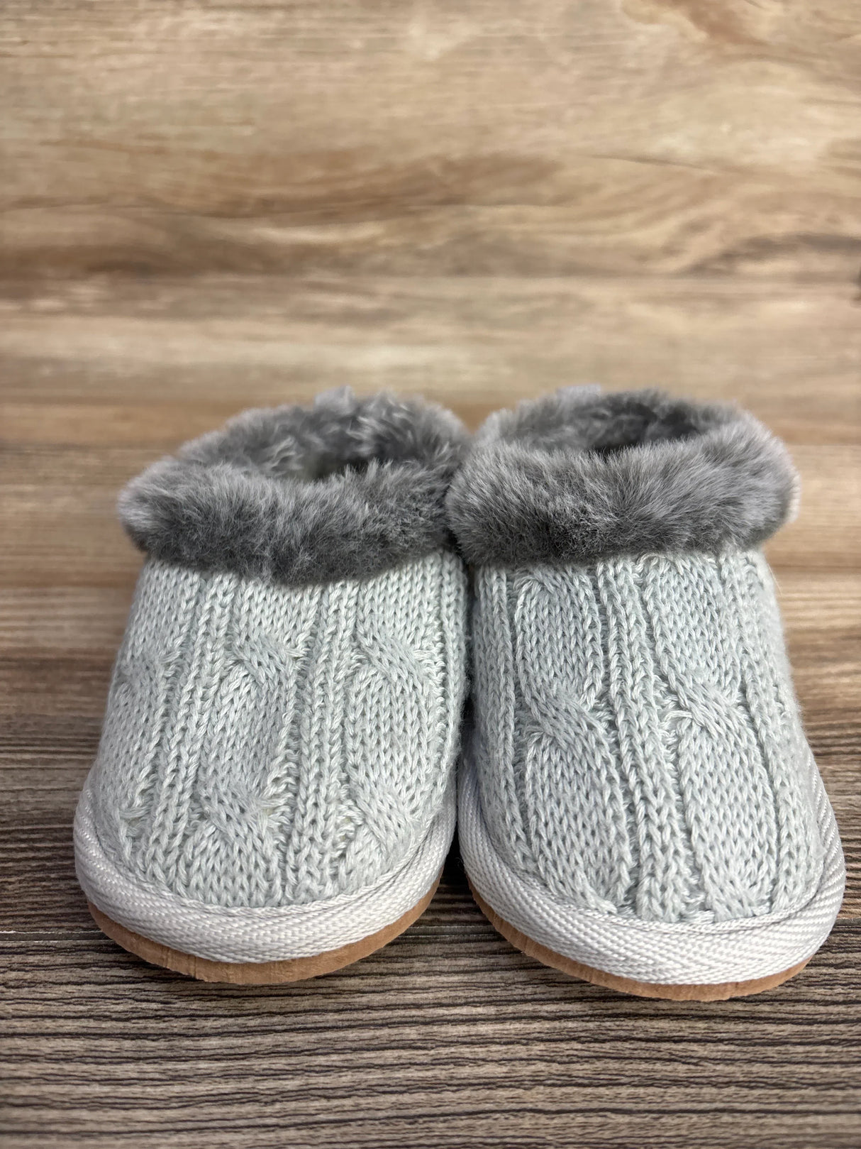 Gray cable knit baby slippers with faux fur lining on wood background