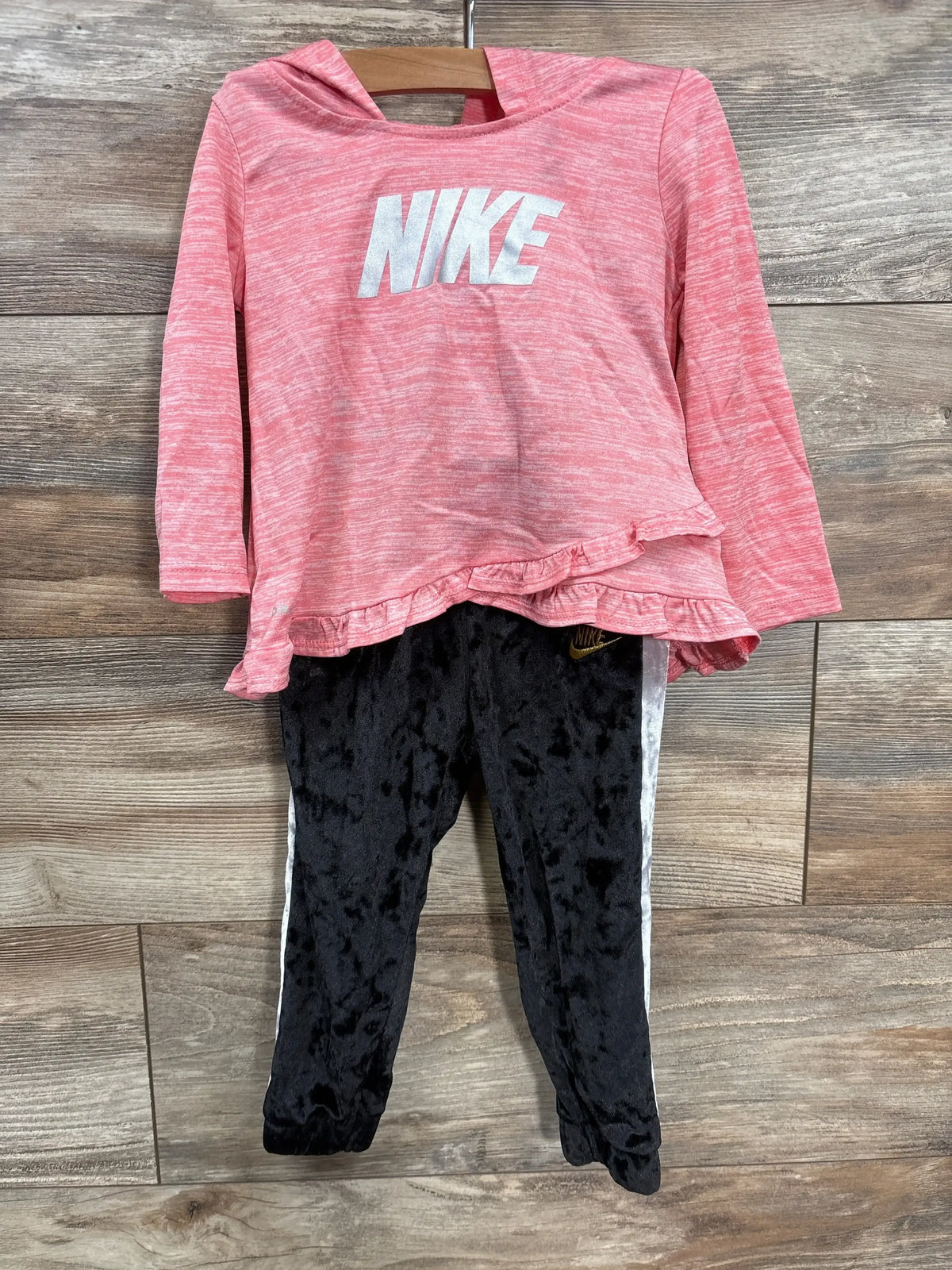 Front view of Nike 2-piece hooded ruffle top and black pants showing white NIKE logo and ruffle hem on wood background