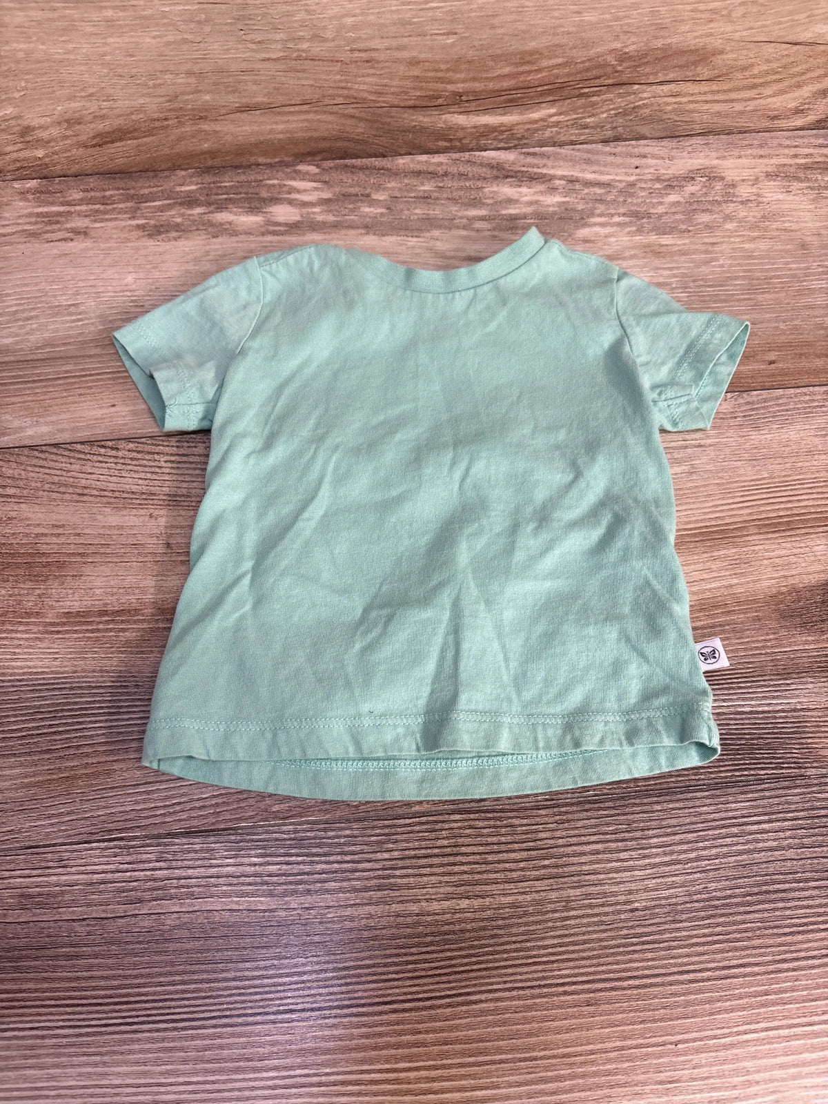Front view of Honest Baby solid green shirt, size 3 to 6 months, with short sleeves on wood-grain background