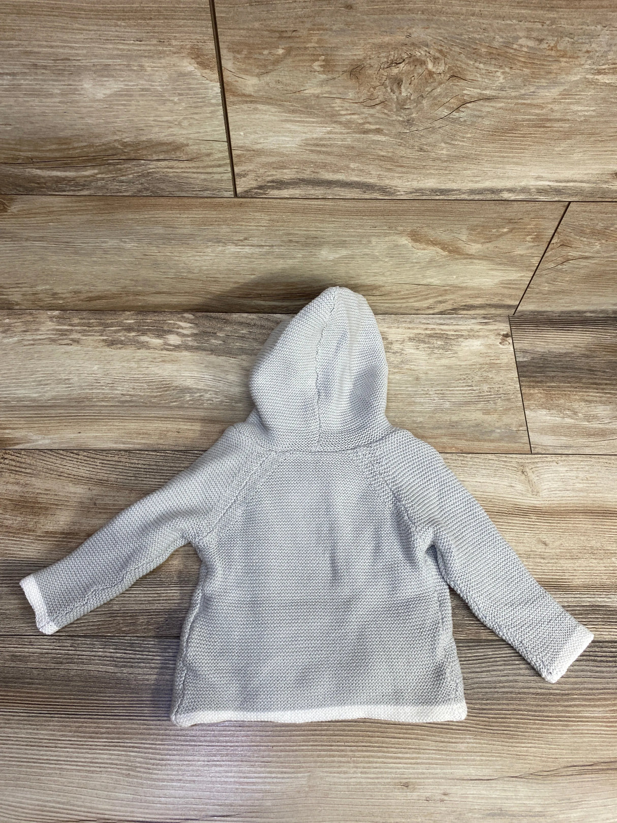Light gray knitted baby hoodie with long sleeves laid flat on wooden floor