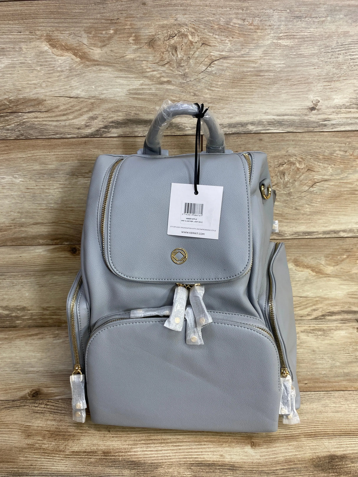 Gray faux leather diaper backpack with gold zippers on wood background, new with tags