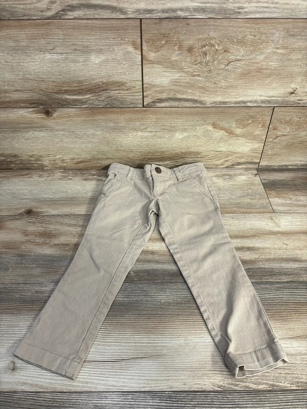 Front flat lay of khaki Old Navy skinny stretch toddler pants showing button waist and slim legs on wood plank background
