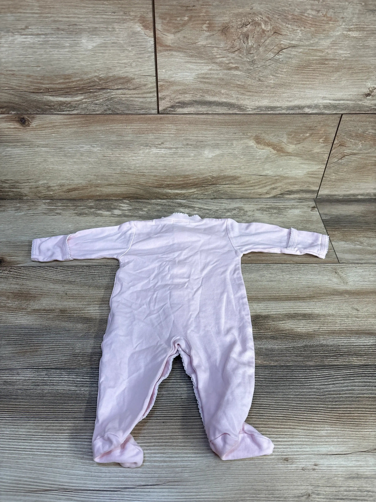 Back view of pink Kissy Kissy snap sleeper showcasing long sleeves and footed legs on a wood-look floor