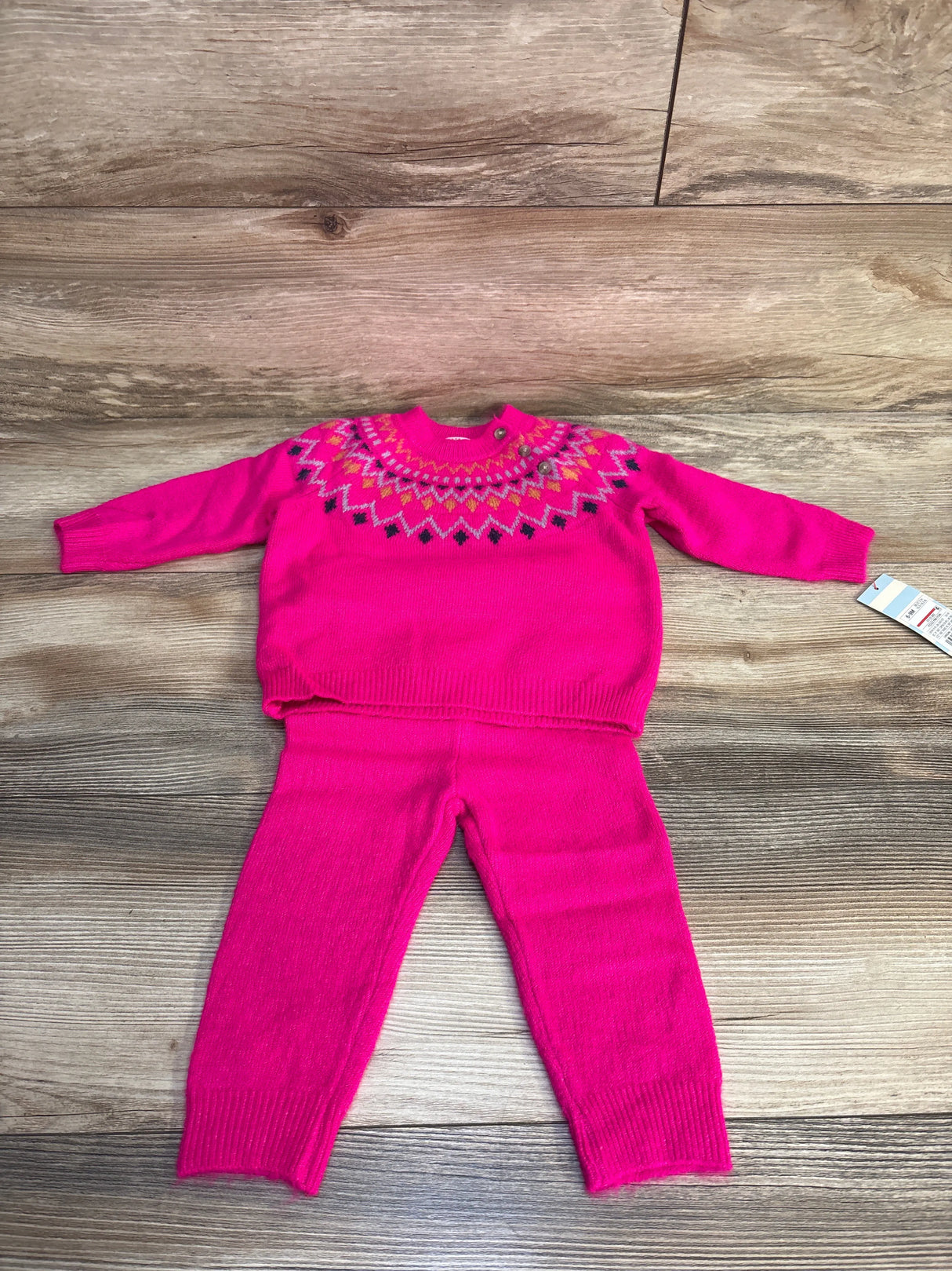 Pink knit toddler sweater and pants set with colorful geometric neckline, laid on wood floor