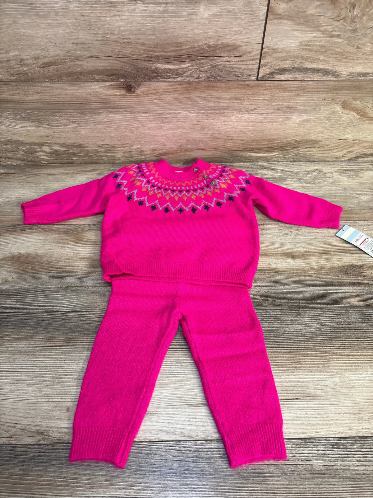 Pink knit toddler sweater and pants set with colorful geometric neckline, laid on wood floor