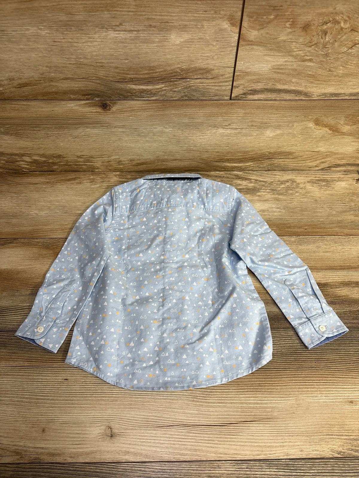 Back view of light blue long-sleeve toddler shirt with white and yellow triangle print on wooden floor