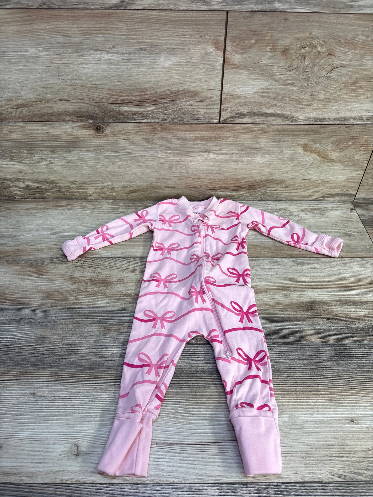 Flat-lay view of pink baby sleeper with bow print, size 3-6 months, showing zipper and fold-over foot cuffs on light wood background