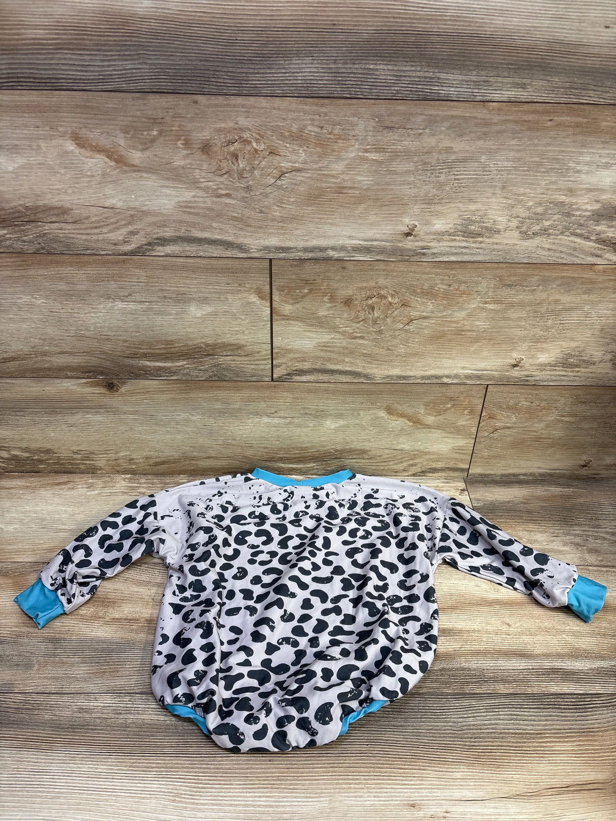 Long-sleeve bubble romper with black leopard print and turquoise trim, laid flat on a wood background