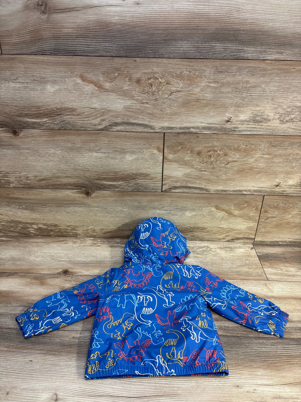 Back view of Cat & Jack 12-month blue windbreaker with multicolor dinosaur print and hood on wood background