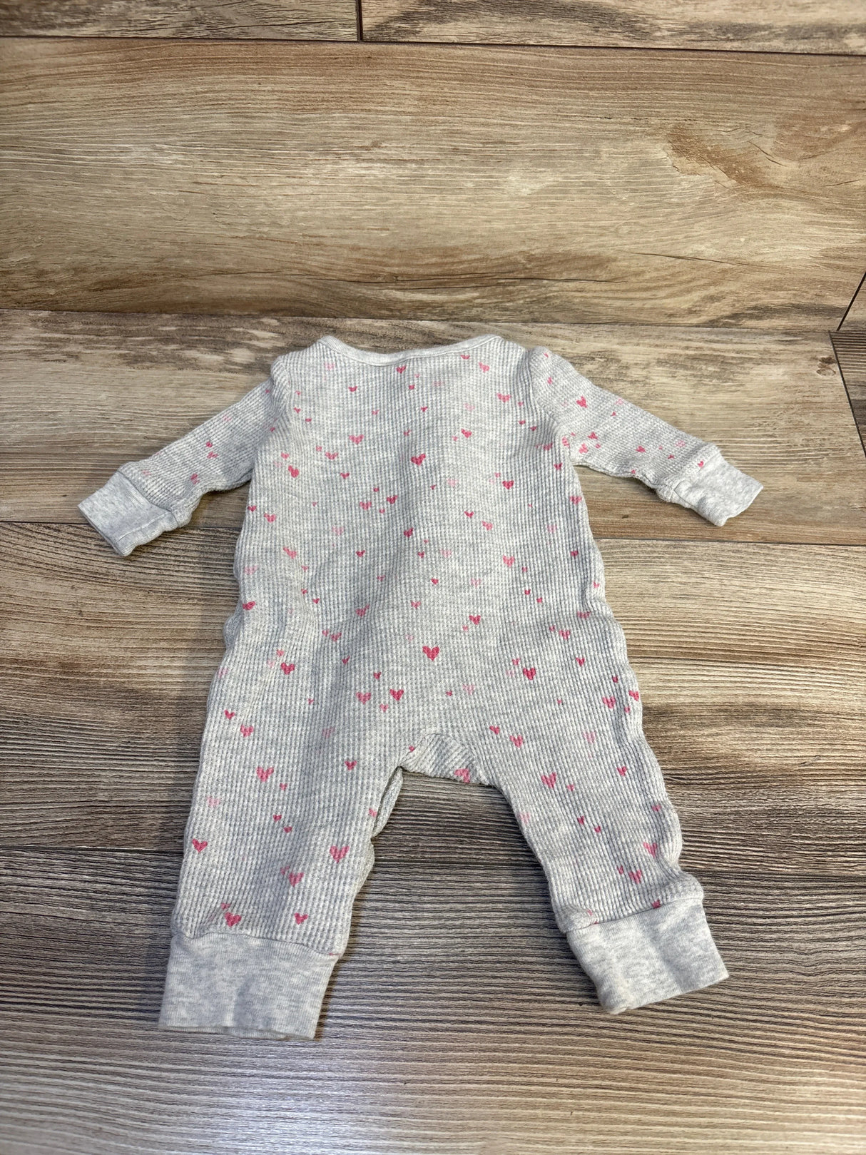 Gray ribbed baby sleeper with pink heart print, long sleeves and cuffs on wooden floor