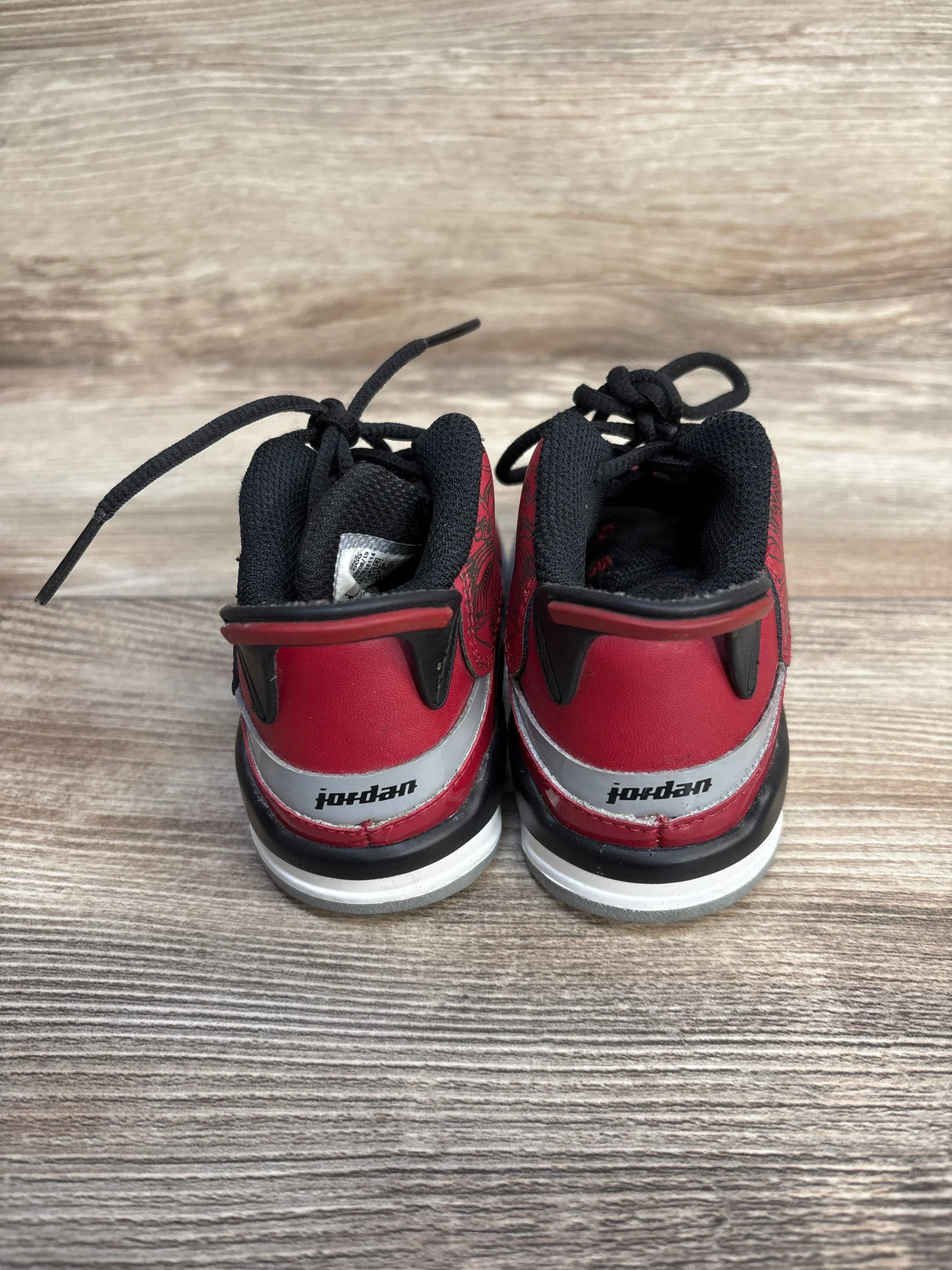 Rear view of Air Jordan Dub Zero TD Toro Bravo toddler sneakers with red and black heel and Jordan logo on wood background