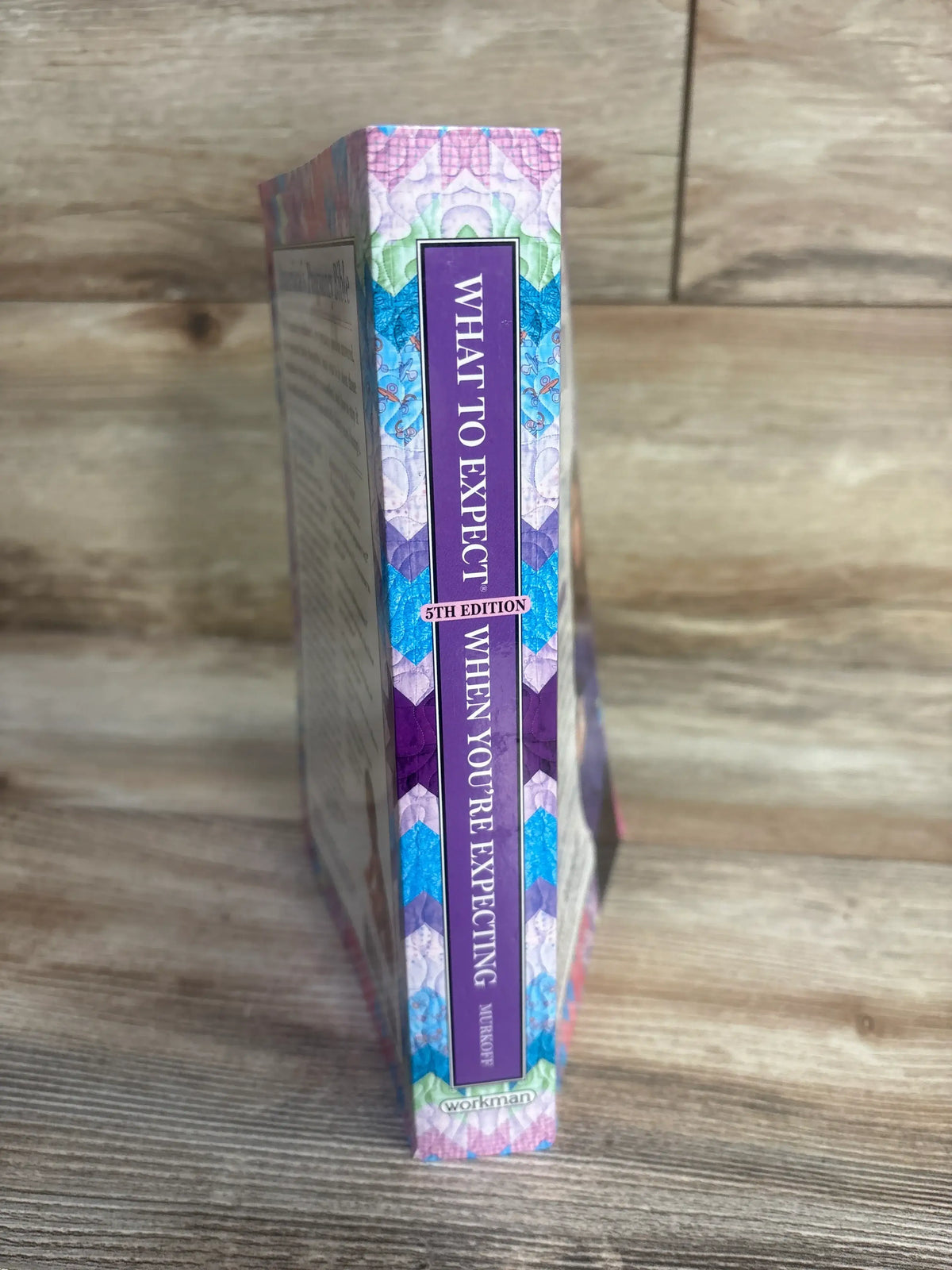 Spine view of What to Expect When You’re Expecting 5th Edition paperback showcasing a colorful patterned cover on a wooden surface