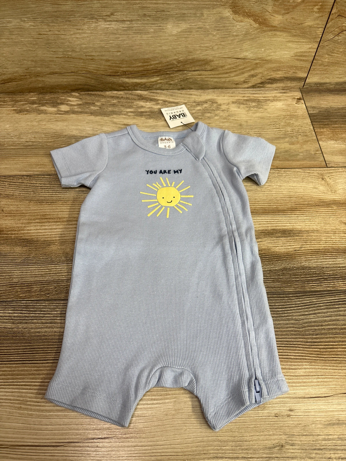 Front view of blue ribbed short sleeve zip romper showcasing a yellow smiling sun graphic on a wood background